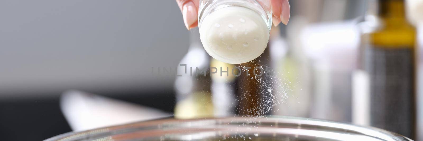 Chef pours salt into a saucepan with food, hands close-up by kuprevich