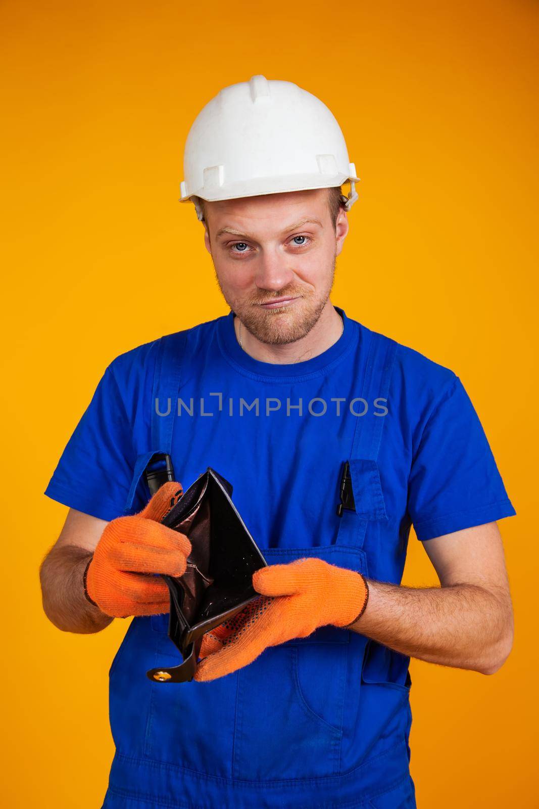 Overweight worker in a protective helmet shows an empty wallet. Recession in the economy. A man in a jumpsuit without money. Recession and the economic crisis, unemployment.