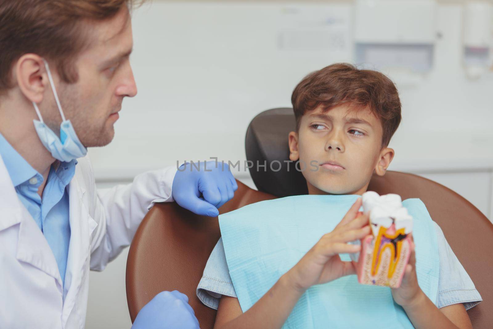 Caries, unhealthy teeth concept. Young boy looking at the dentist suspiciously, preparing for his caries dental treatment at the clinic