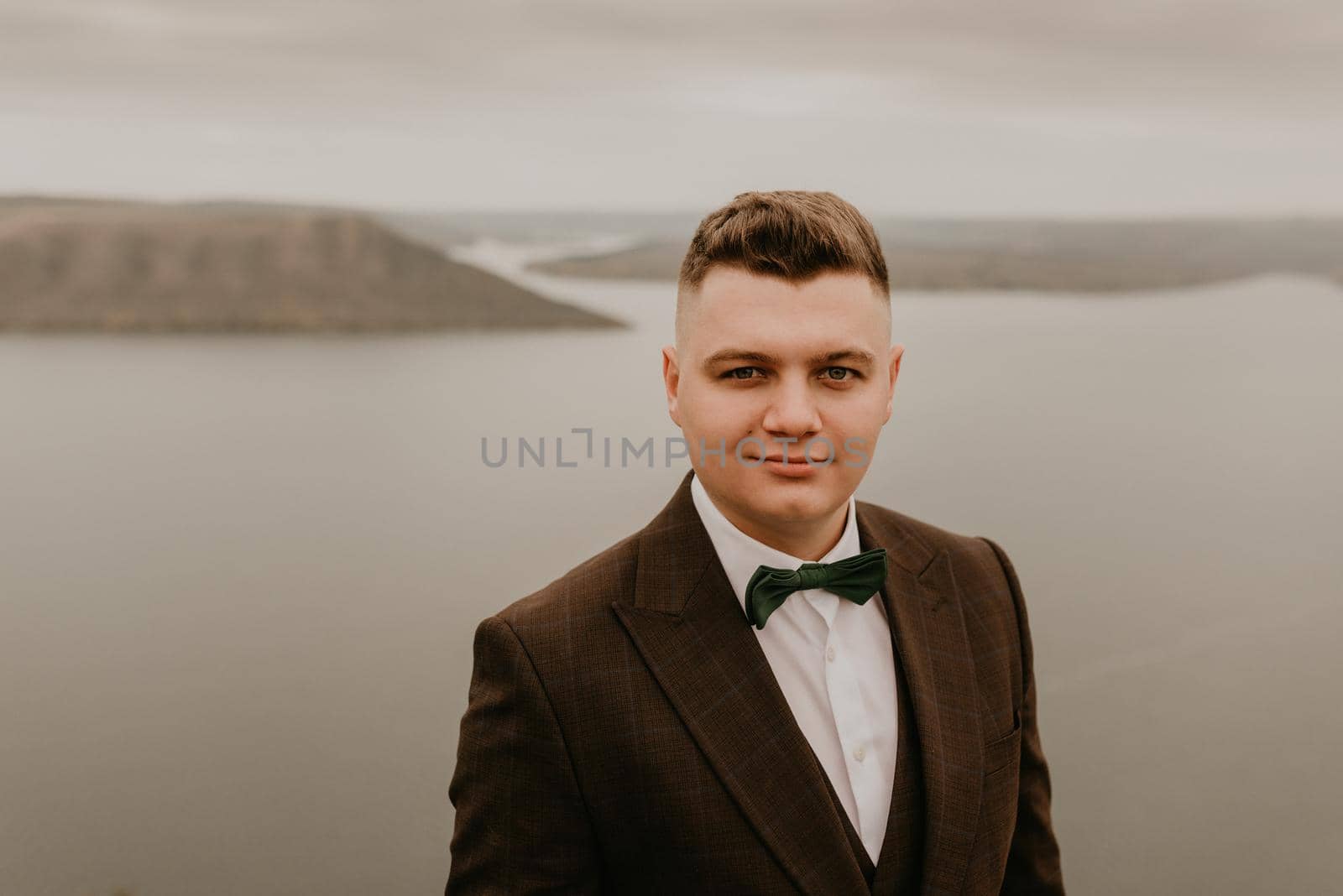 adult man with short hair in classic suit, white shirt, bow tie on neck. lonely person in nature outdoor. panoramic view big river lake sea in distance silhouettes of islands. bakota ukraine