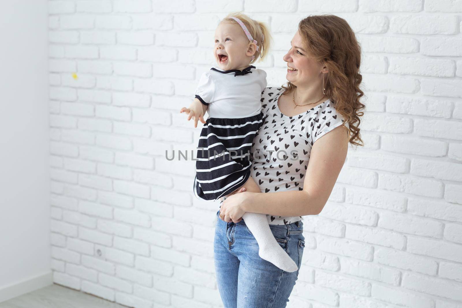 Mother holds and having fun child with hearing aids and cochlear implants on white brick wall with copy space . Deaf and diversity and innovating medicine technologies concept by Satura86