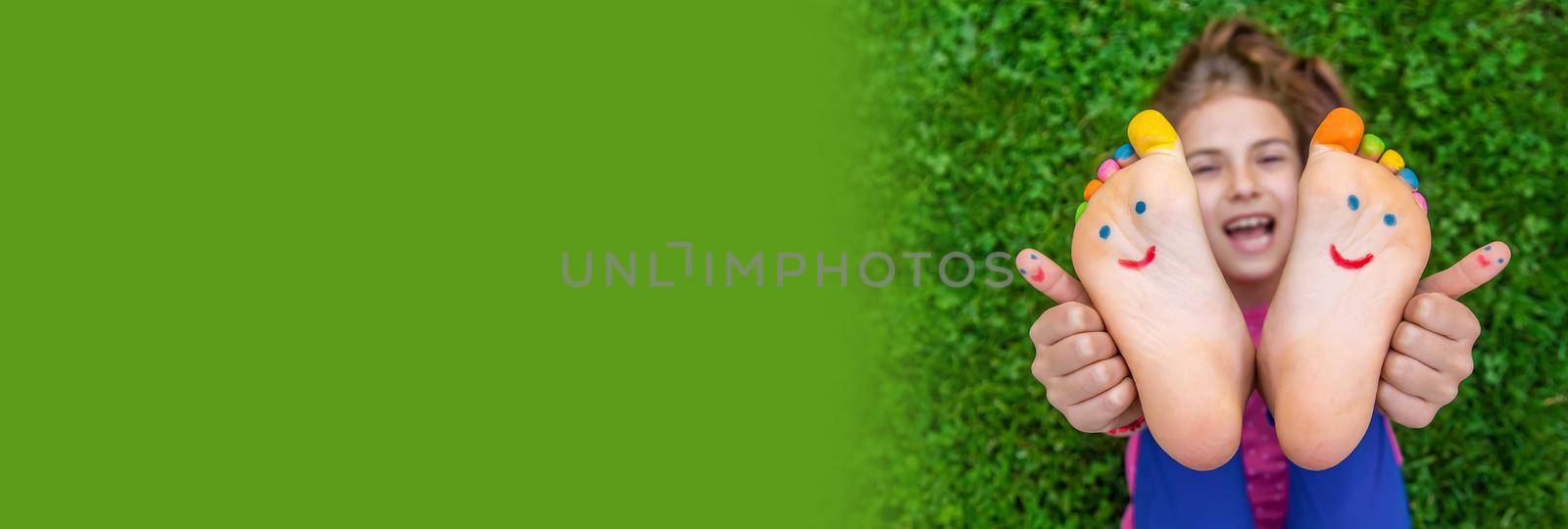 Feet of a child on the grass with a painted smile. Selection focus. by yanadjana