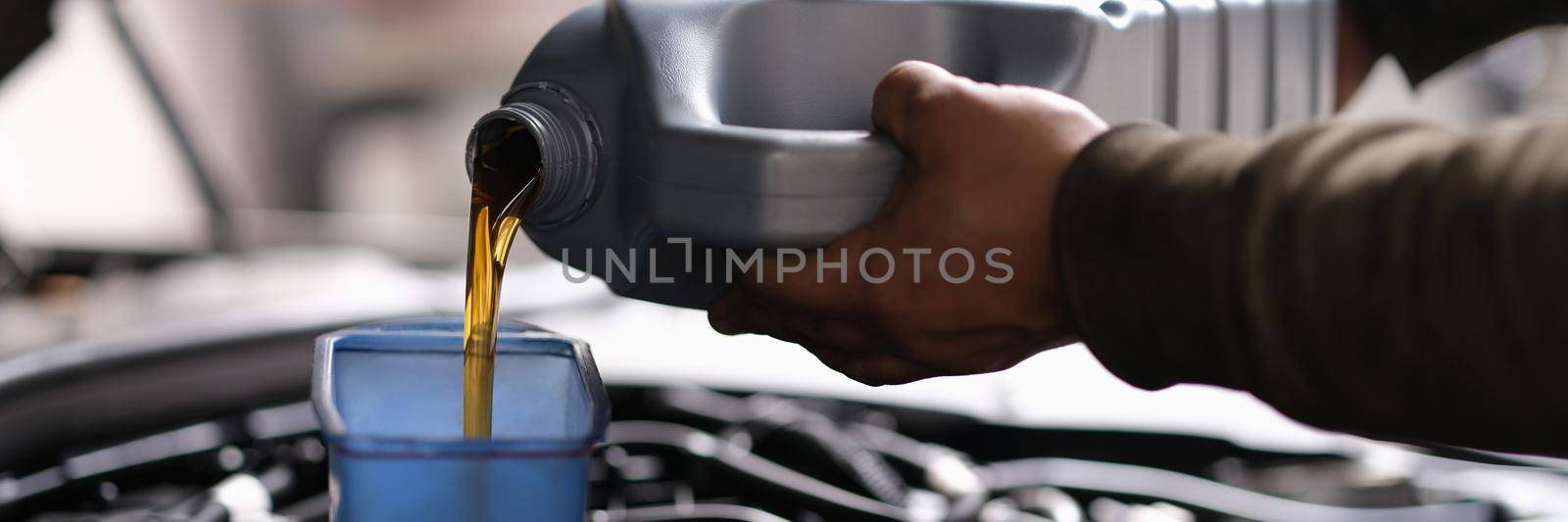 A man is pouring oil into the car from a canister, close-up. Garage engine maintenance, machine oil change, automobile