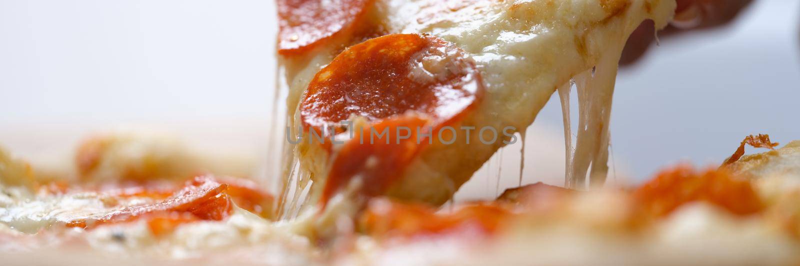 Hand takes a large slice of hot pizza, close-up by kuprevich