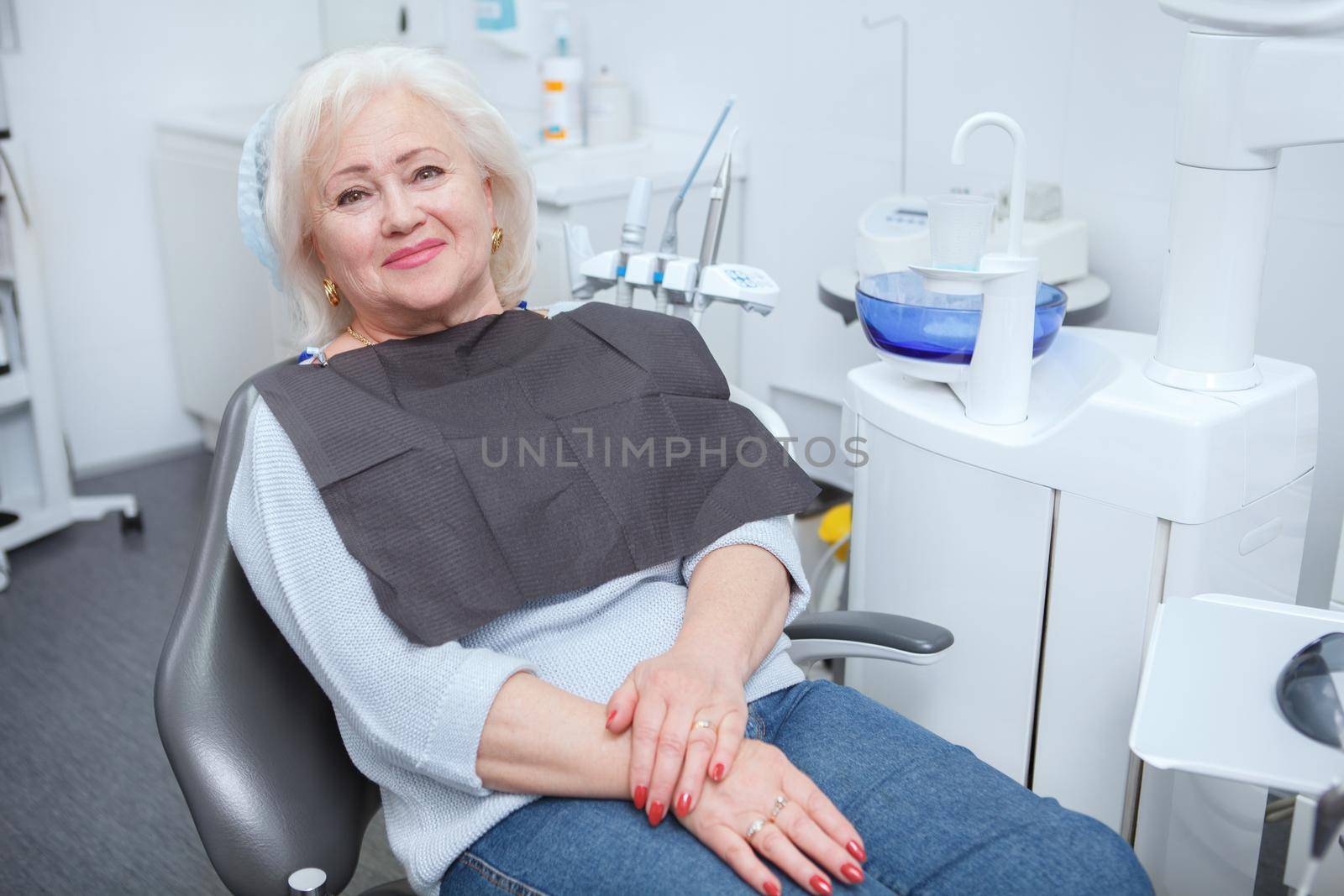 Charming senior woman smiling to the camera, sitting in dental chair at the clinic