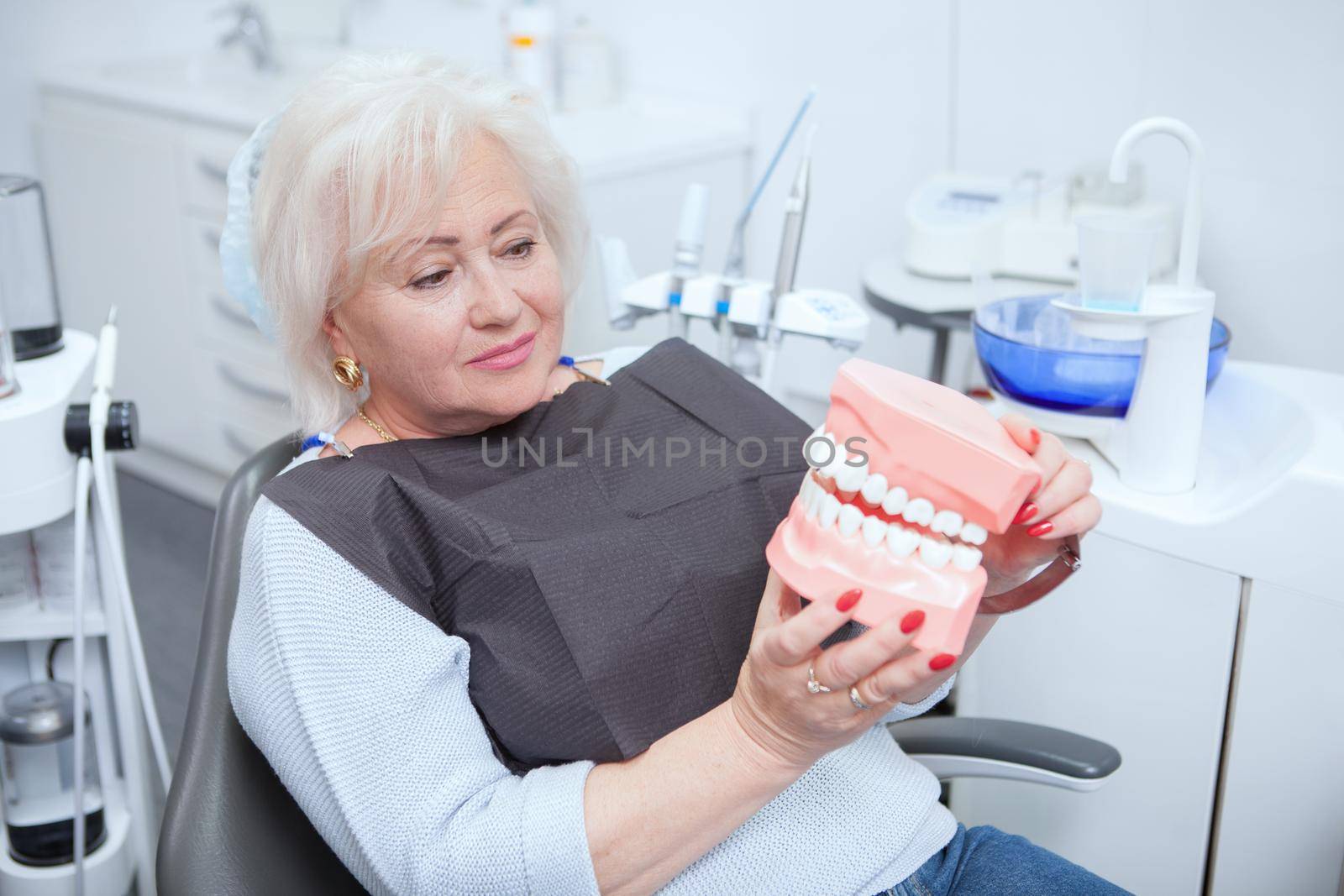 Elderly female patient looking at jaw model, sitting in dental chair