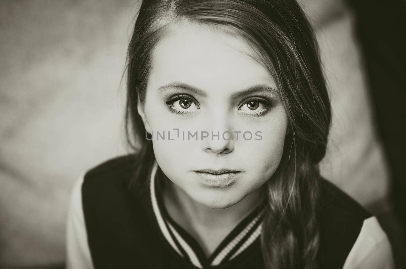 Black and white photo of a young teenage girl looking directly at the camera. Evening makeup for stage performances. dimple on the cheek, hair in a plait, large painted eyes, plump lips, straight nose