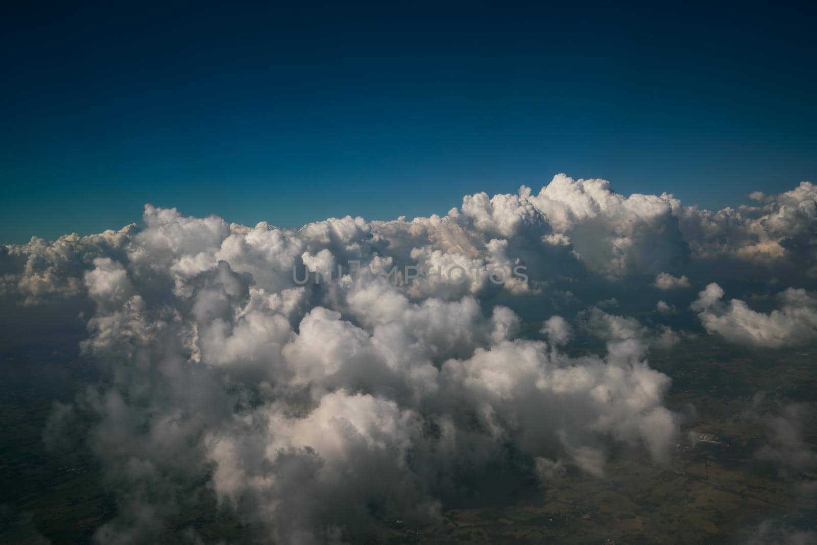 Earth landscape viewed from airplane. Earth surface under the white clouds and blue sky from aerial view. Cloudy weather covering residential land and argriculture land.
