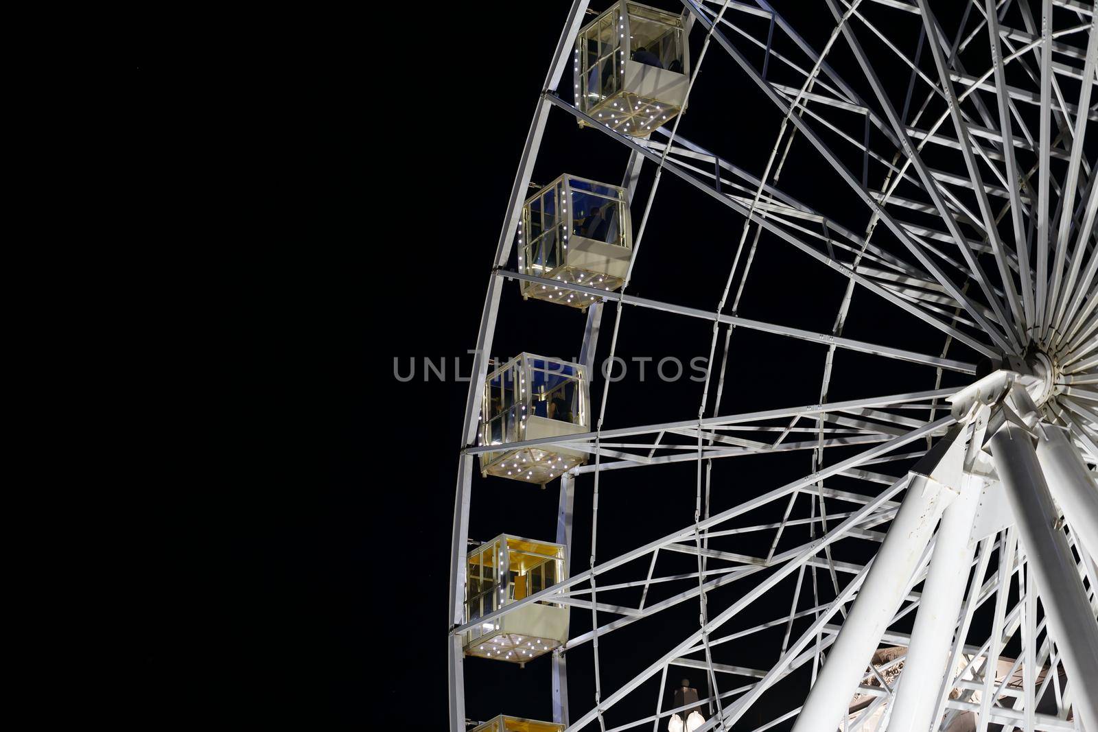 Illuminated white Ferris wheel against the black night sky by clusterx
