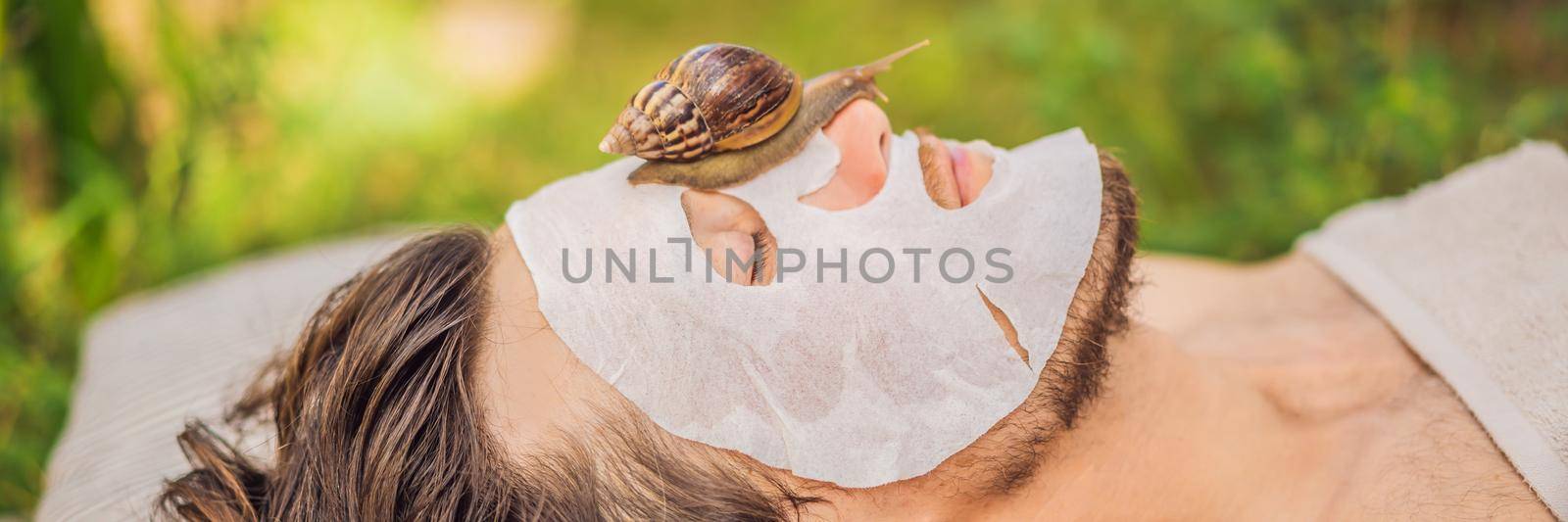 Young man makes a face mask with snail mucus. Snail crawling on a face mask. SPA for man, SPA for all. BANNER, LONG FORMAT