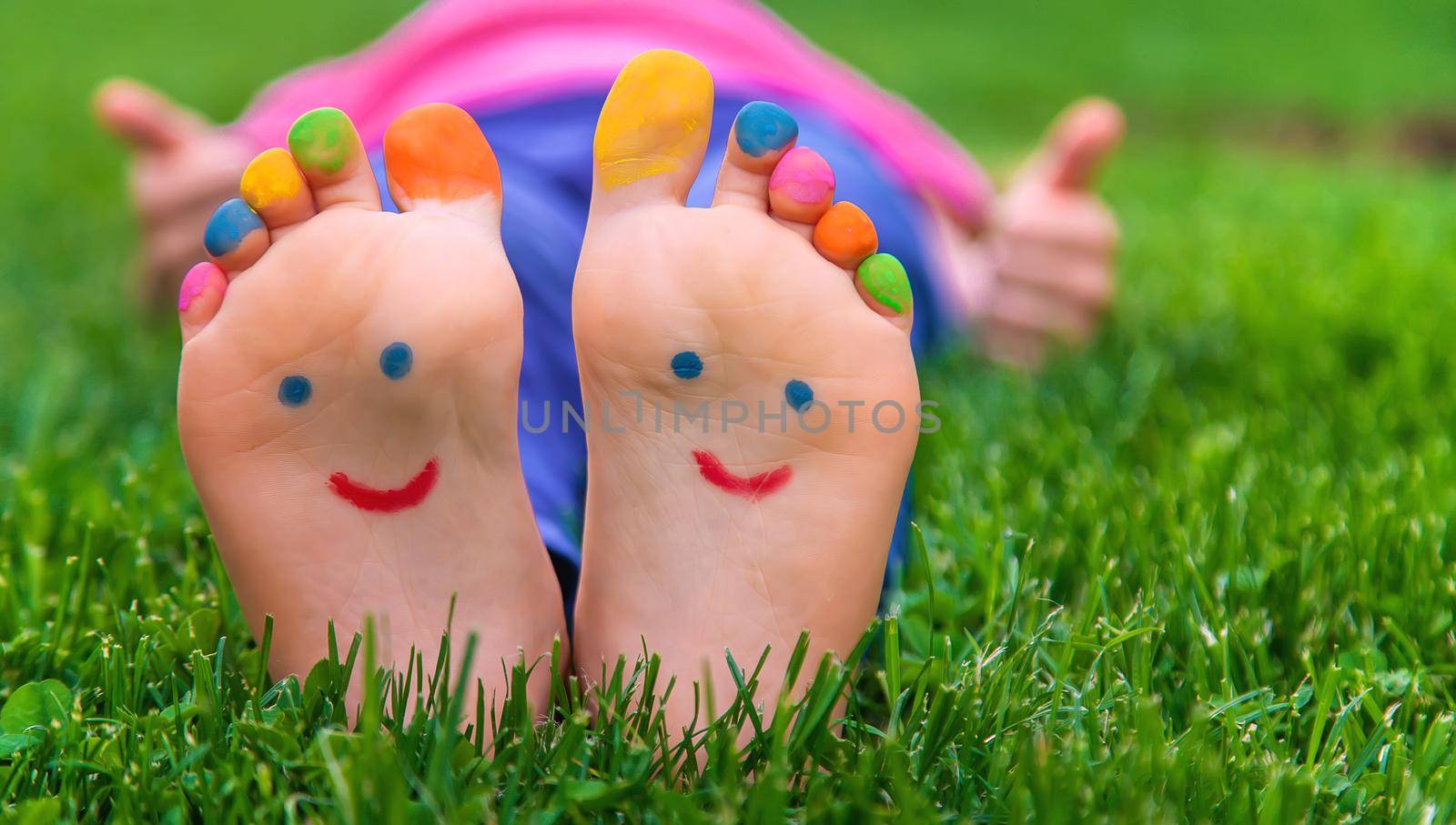 Feet of a child on the grass with a painted smile. Selection focus. Kid.