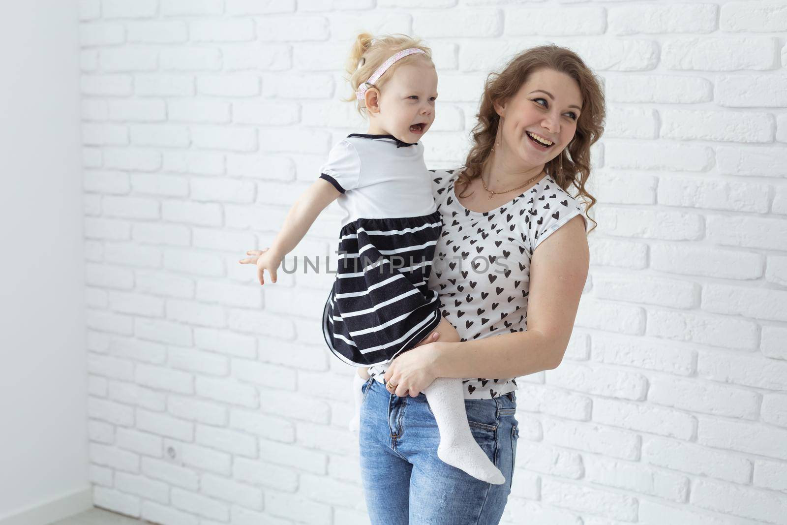 Mother holds and having fun child with hearing aids and cochlear implants on white brick wall with copy space . Deaf and diversity and innovating medicine technologies concept by Satura86