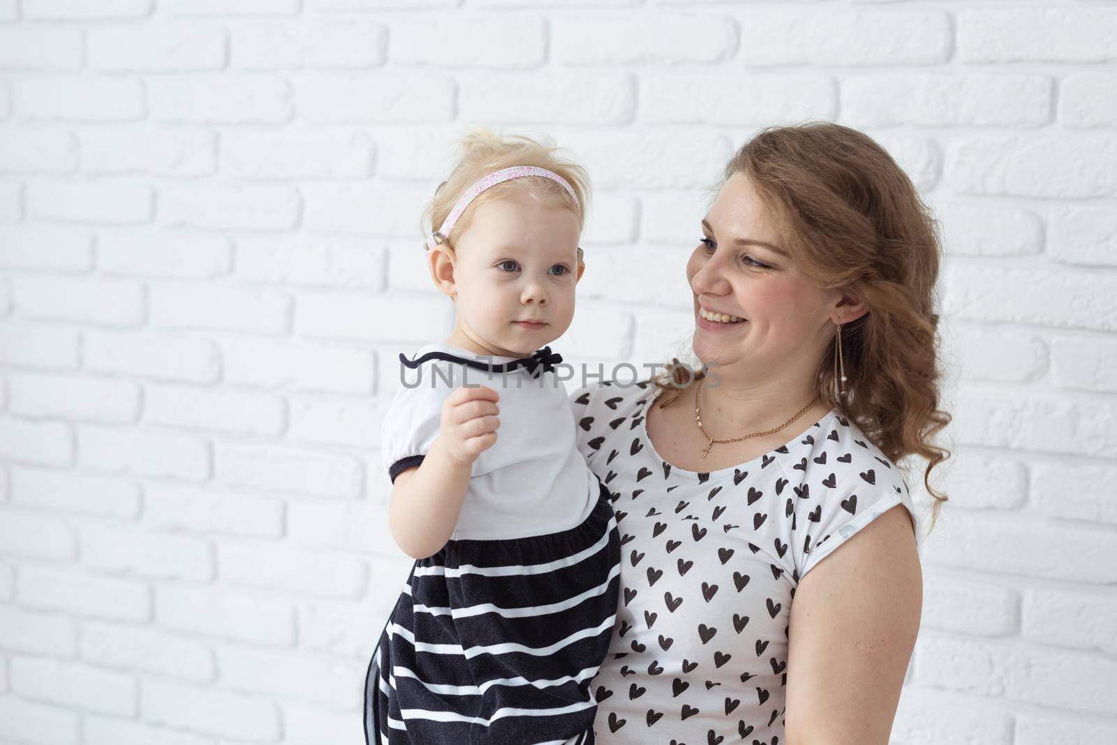 Mother helps her deaf baby daughter putting hearing aid in little girl's ear indoors - cochlear implant and innovative medical technologies