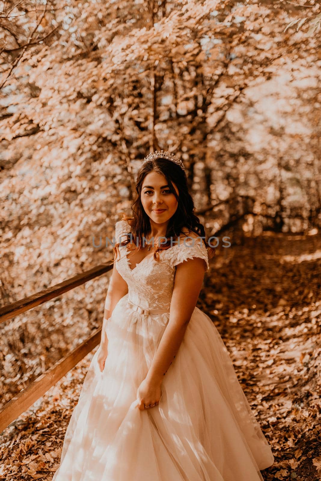 woman bride in white wedding dress with hairstyle makeup and crown on her head walks through autumn forest on fallen orange leaves