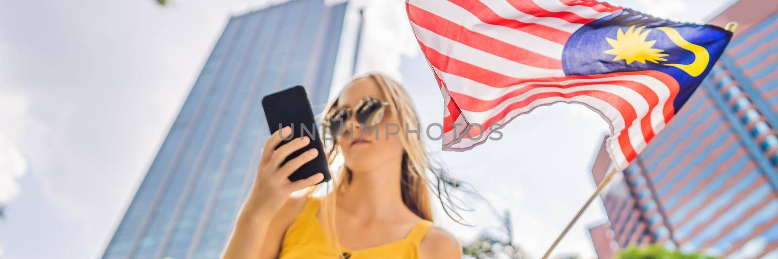 Travel and technology. Young woman tourist with the flag of Malaysia is looking at a city map in a smartphone for navigation. BANNER, LONG FORMAT