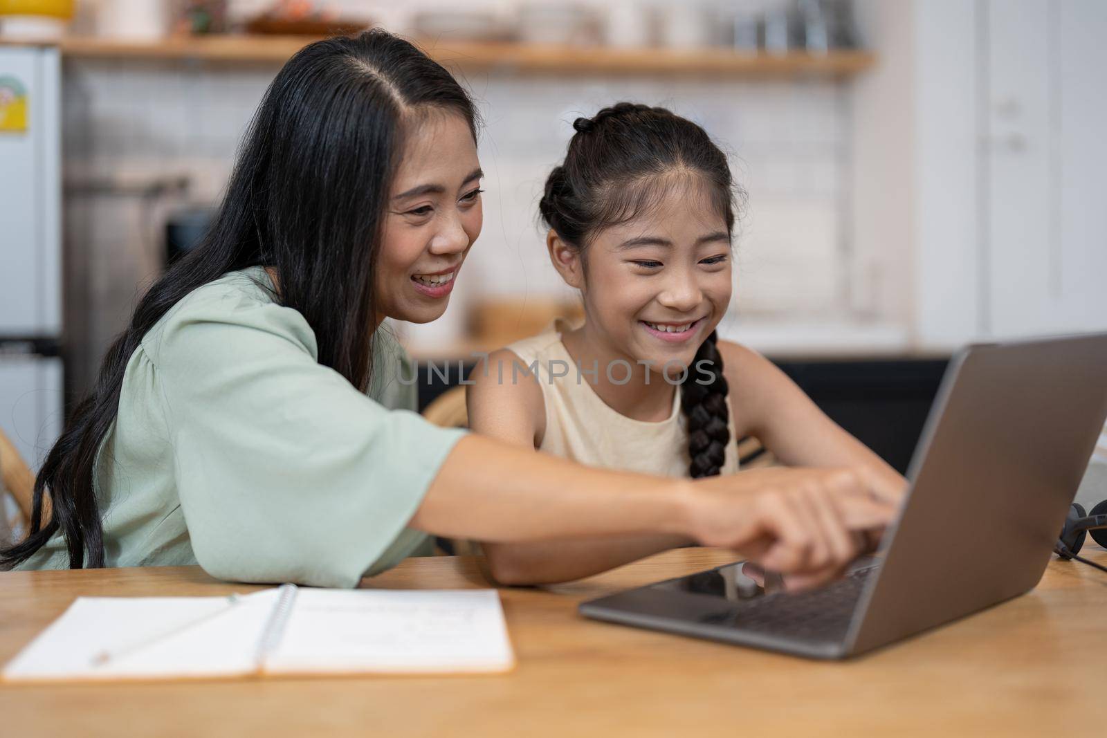 Mother and asian kid little girl online learning on laptop computer making homework studying knowledge with online education e-learning system. children video conference with teacher tutor at home.