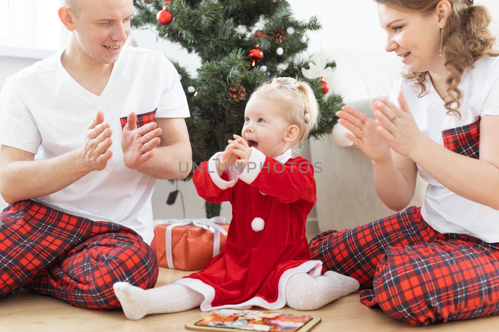 Toddler child with cochlear implant plays with parents under christmas tree - deafness and innovating medical technologies for hearing aid by Satura86