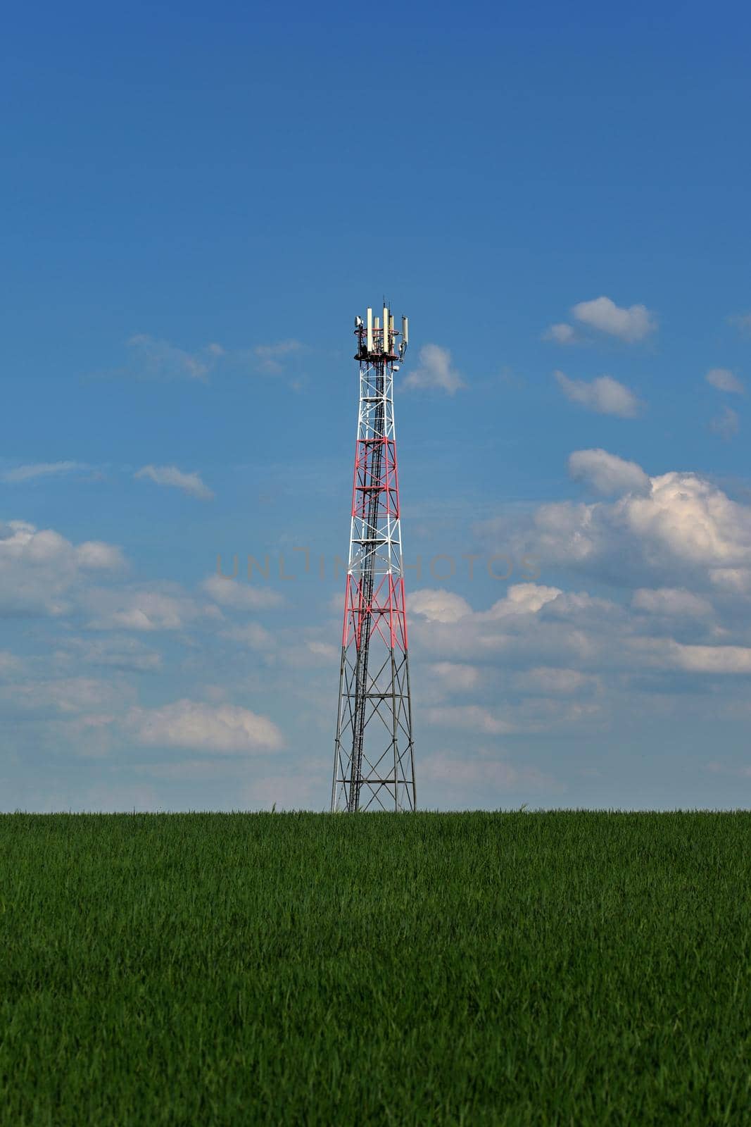 Telecommunication Tower - Transmitter for gsm signal of mobile phones in the field. In the background blue sky with clouds. Concept for modern technology and industry. by Montypeter