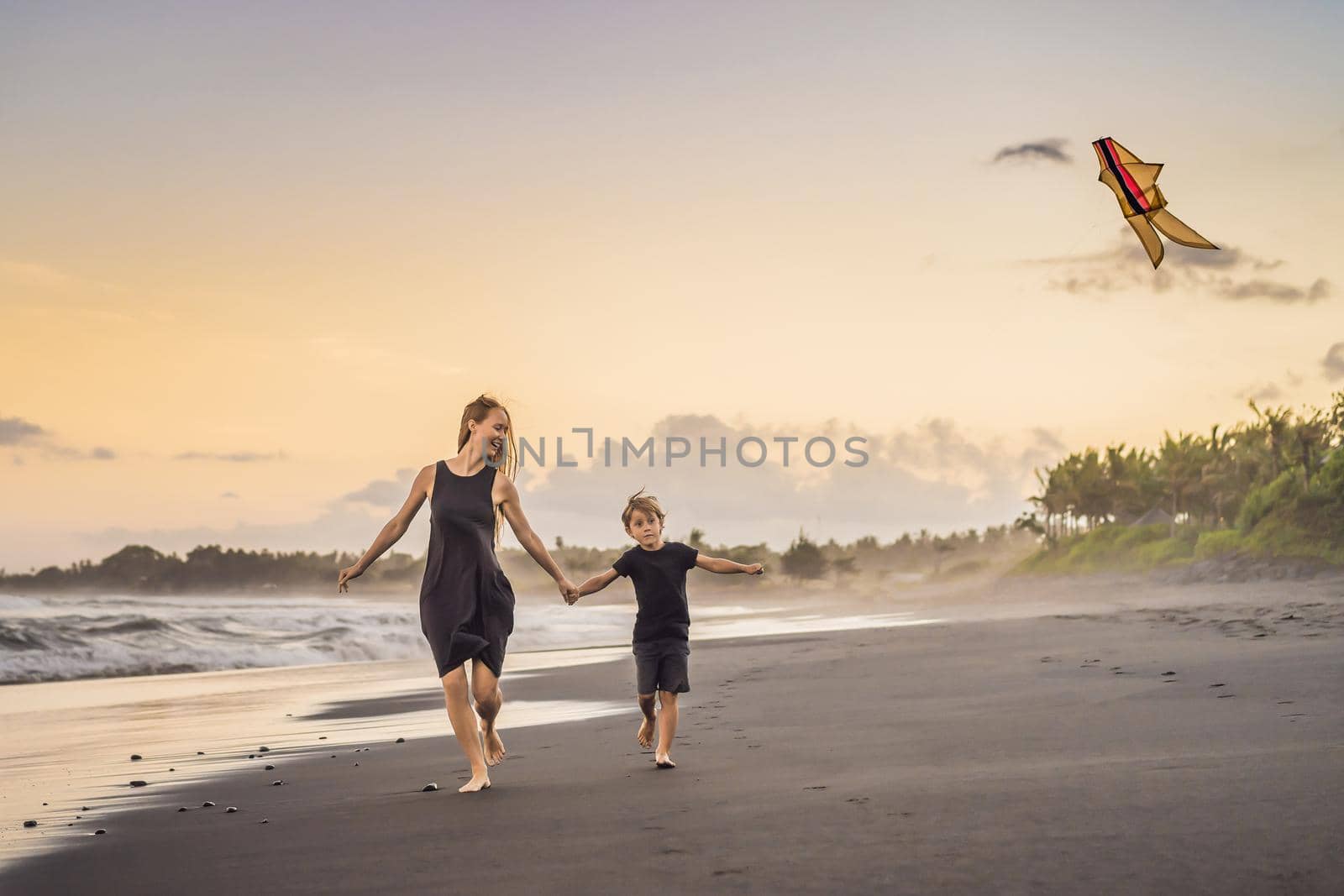 Mom and son are running on the sea beach launching a kite.