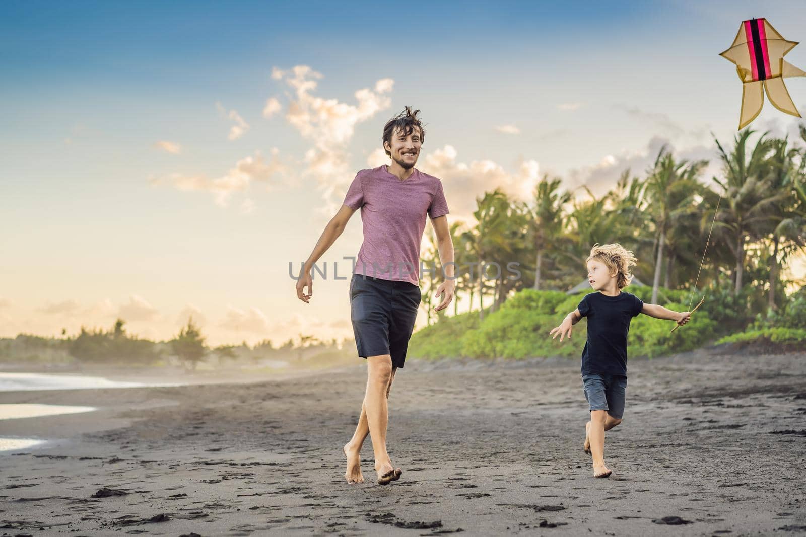 Young father and his son running with kite on the beach.