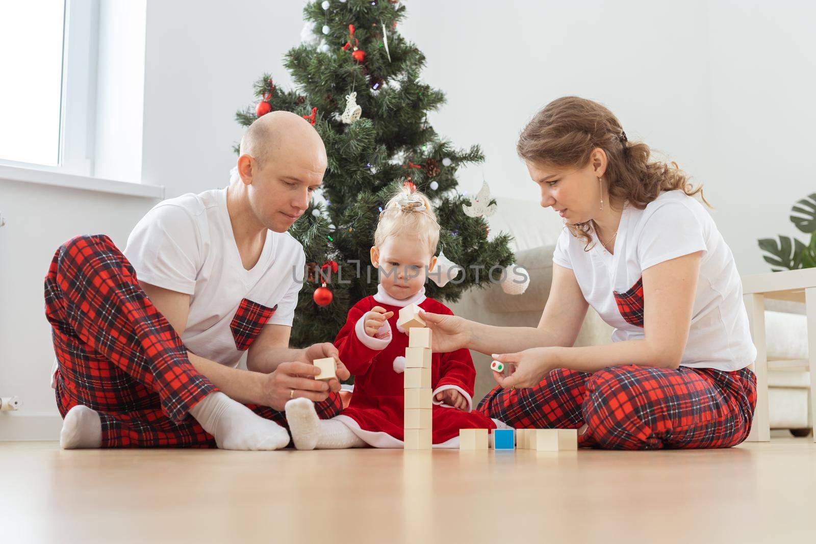 Toddler child with cochlear implant plays with parents under christmas tree - deafness and innovating medical technologies for hearing aid by Satura86