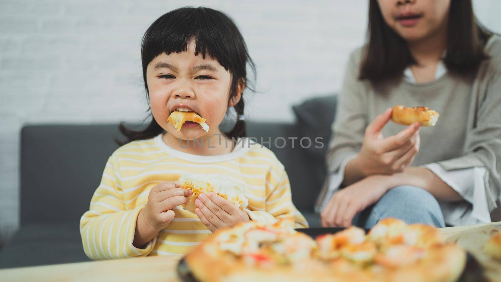 Asian mothers and children do activities at home. Mother is going to feed pizza for her kids. Children are eating and tasting italian homemade pizza.