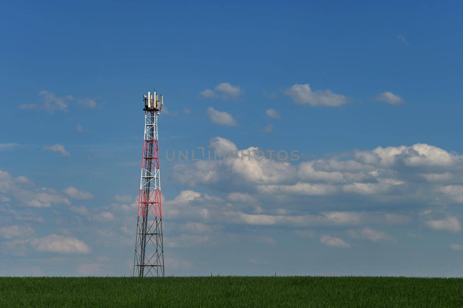 Transmitter for gsm signal of mobile phones in the field. In the background blue sky with clouds. Concept for modern technology and industry - Telecommunication Tower.