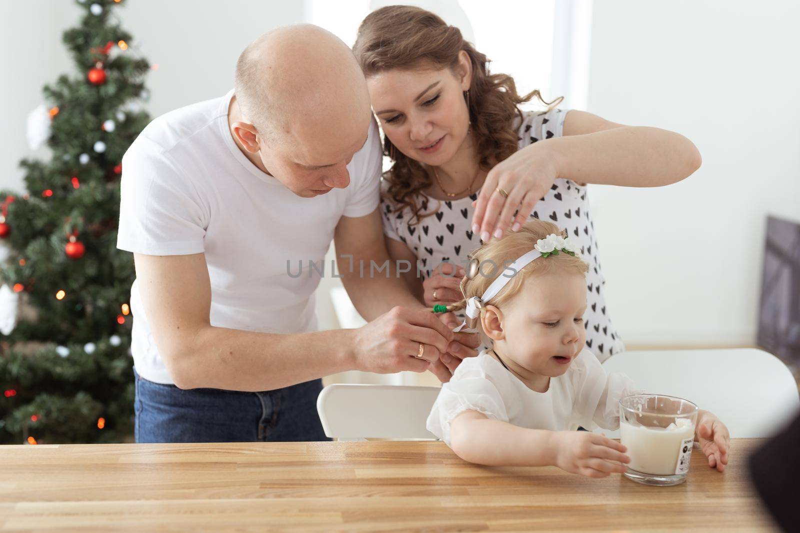 Mother and father helps to put on cochlear implant for their deaf baby daughter in christmas living room. Hearing aid and innovating medical technologies treatment deafness concept by Satura86