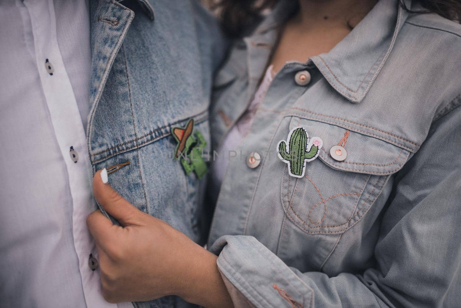 pair of young people a man and a woman dressed in white wedding clothes denim blue jackets.Mexican people on a snowy white background.boutonnieres green small fabric cactus badges.Dark tanned hands