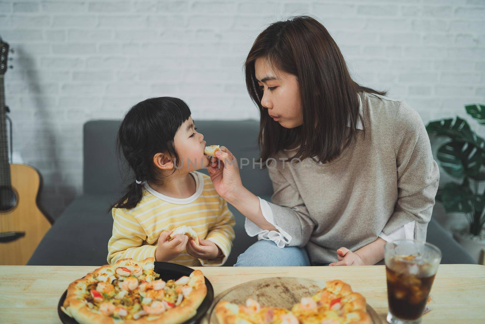 Asian mothers and children do activities at home. Mother is going to feed pizza for her kids. Children are eating and tasting italian homemade pizza.  by Wmpix