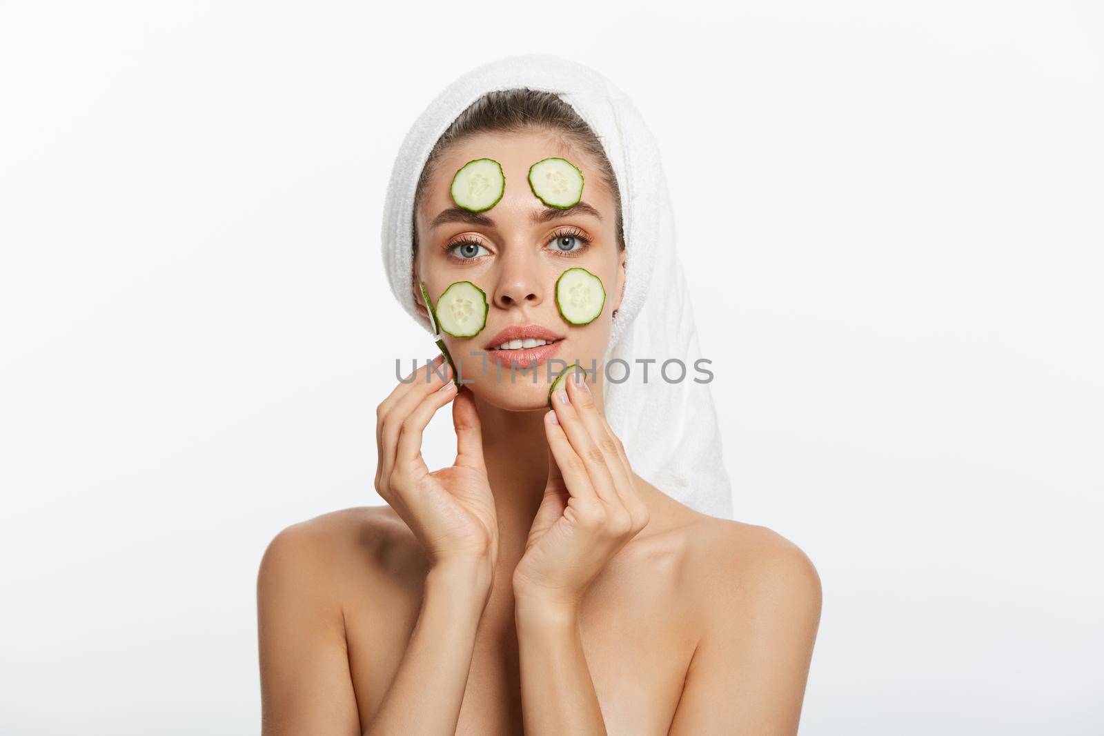 Woman with facial mask and cucumber slices in her hands on white background.