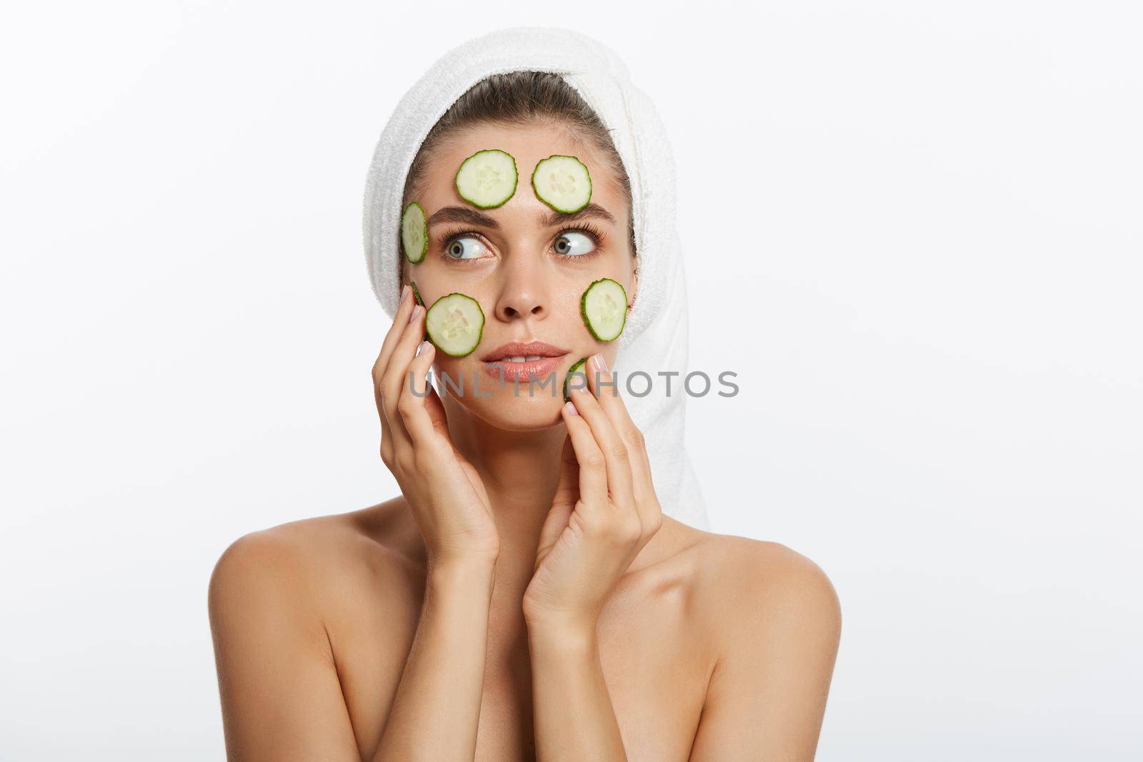 Woman with facial mask and cucumber slices in her hands on white background.