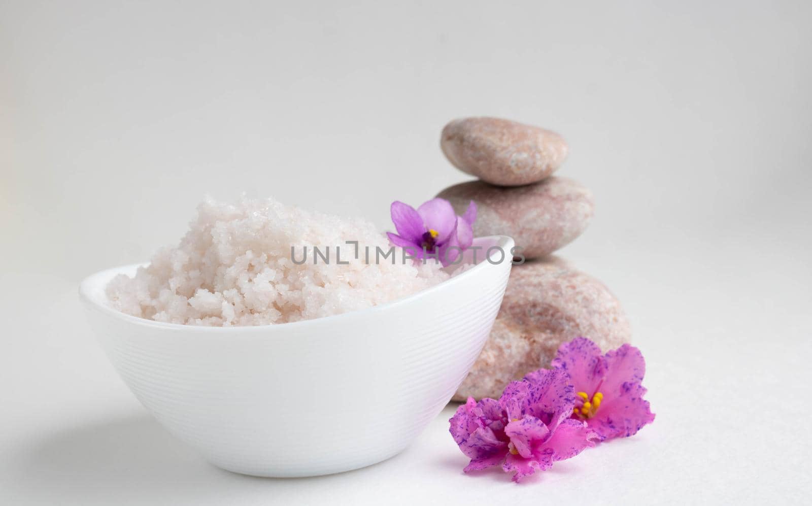 White bowl with pink salt, flowers and stones on a white background