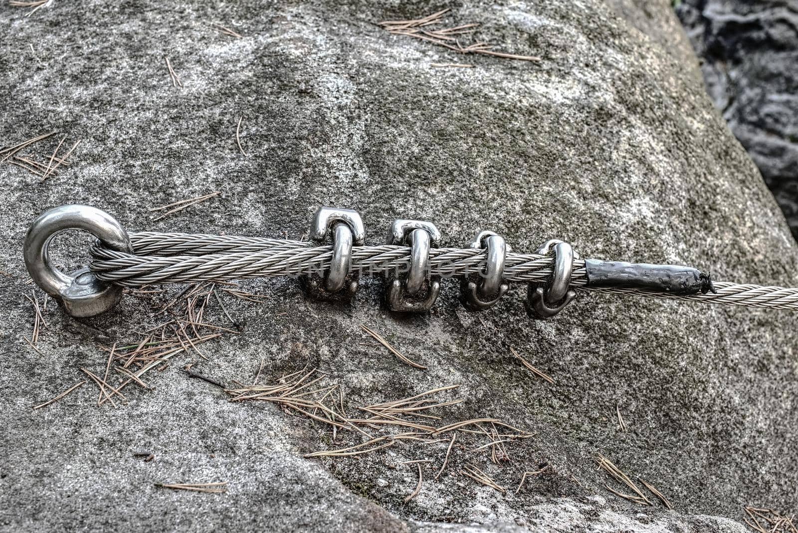 Climbing carabiner attached to cliff rock.  Detail of via ferrata steel cable attached to stainless iron rod on mountain top Shallow depth of field.
