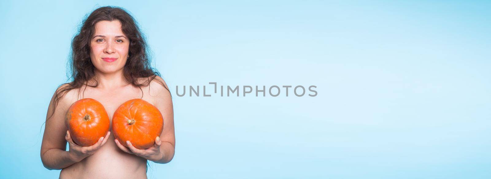 Breasts implant banner concept - Happy woman holding two pumpkins in front of her breasts on blue background with copy space and place for advertising by Satura86