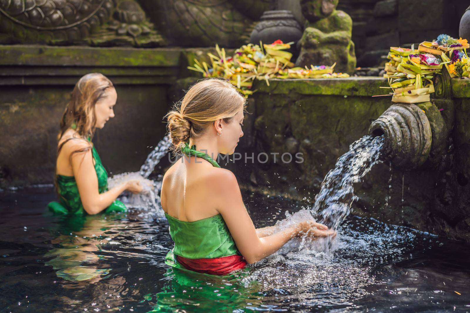 Two women in holy spring water temple in bali. The temple compound consists of a petirtaan or bathing structure, famous for its holy spring water by galitskaya