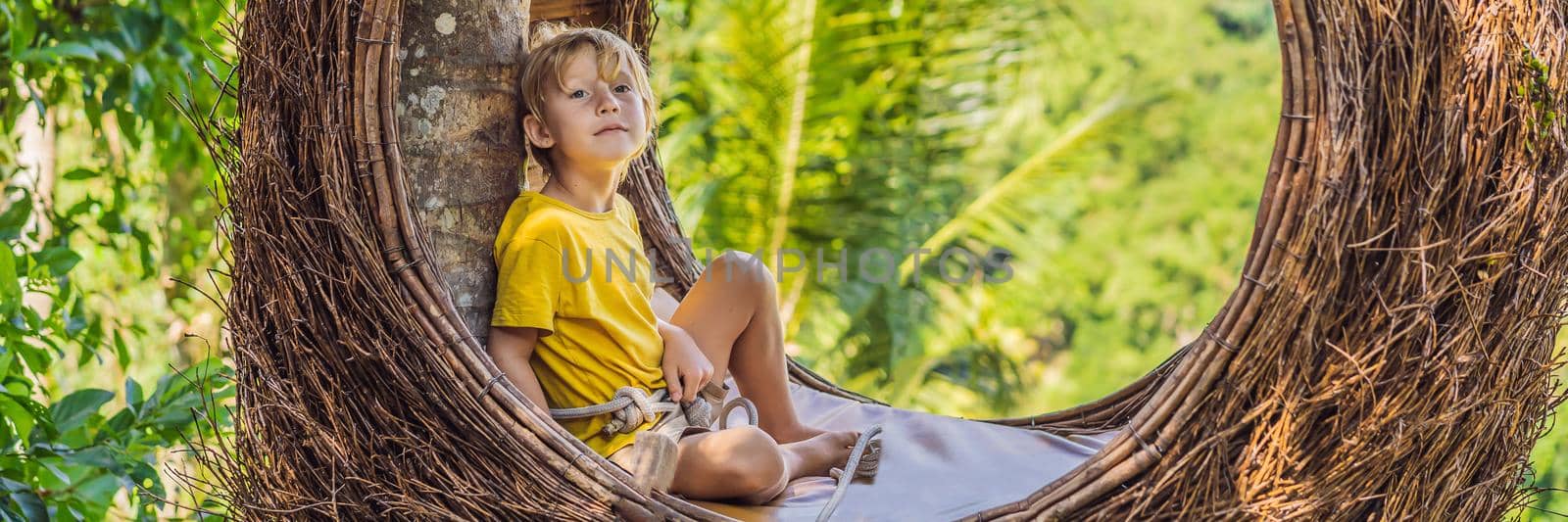 BANNER, LONG FORMAT Bali trend, straw nests everywhere. Child friendly place. Boy tourist enjoying his travel around Bali island, Indonesia. Making a stop on a beautiful hill. Photo in a straw nest, natural environment. Lifestyle. Traveling with kids concept. What to do with children by galitskaya