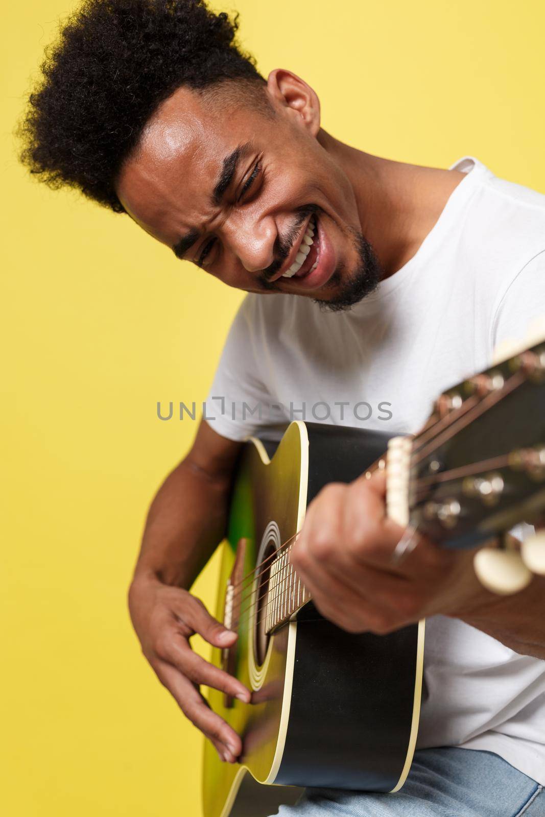 african american retro styled guitarist playing acoustic guitar isolated on yellow gold background.