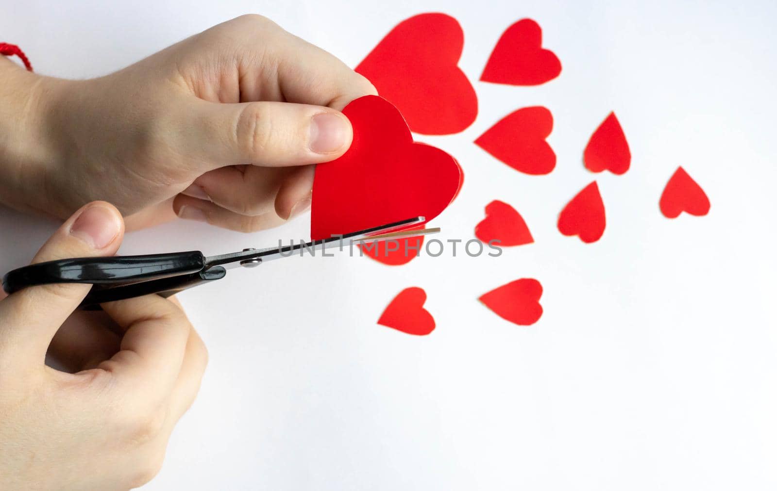 Hands cut out red paper hearts on a white background with scissors. View from above. Valentine's day, mother's day, a symbol of love. Space for copying. by lapushka62