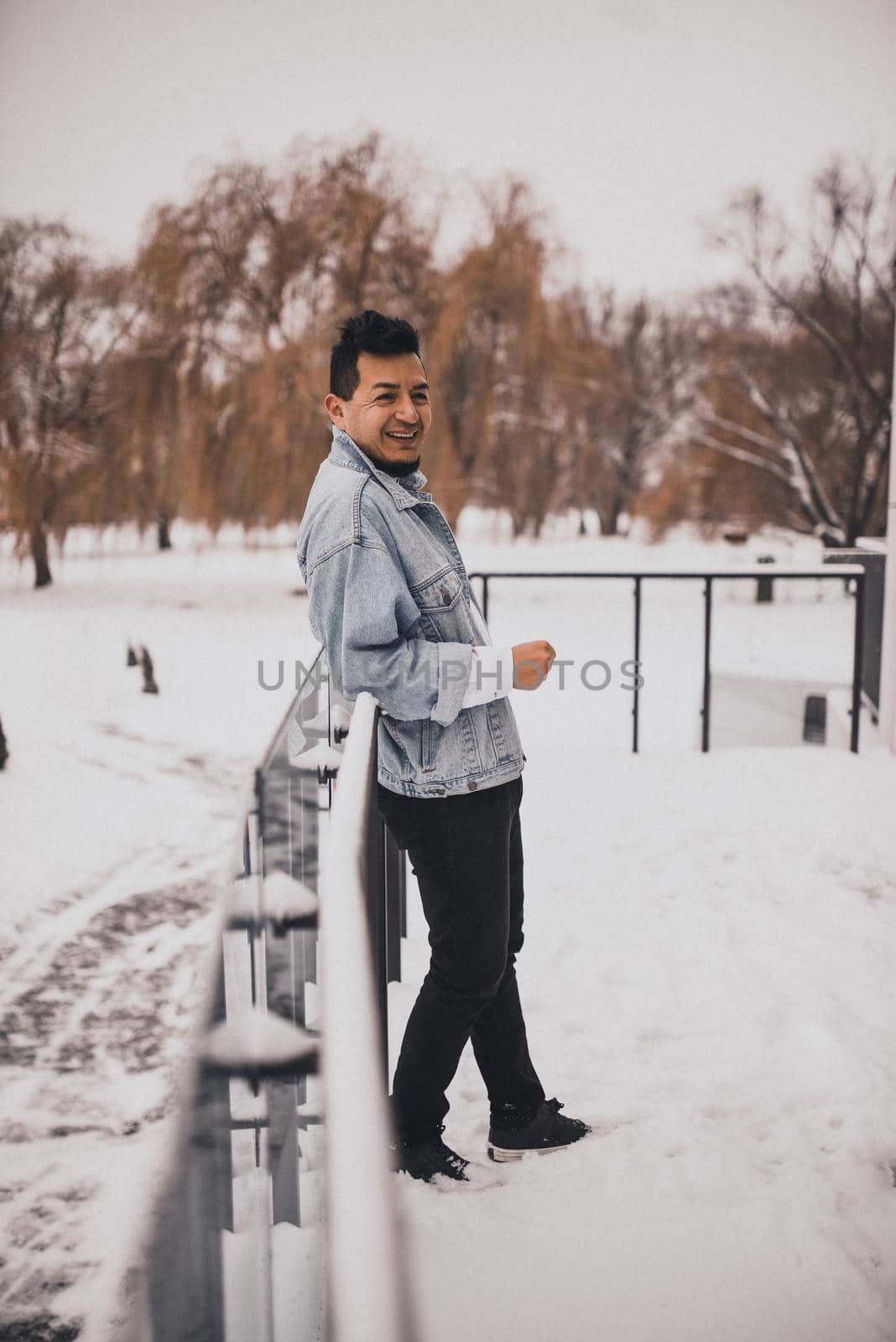Hispanic brunette man with beard in denim jacket in winter in the middle of snow. Men's Street Fashion Casual Style 2021
