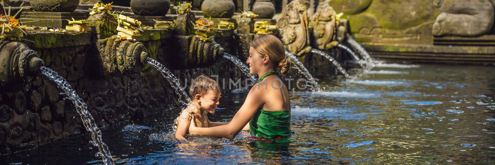 BANNER, LONG FORMAT Mother and son in holy spring water temple in bali. The temple compound consists of a petirtaan or bathing structure, famous for its holy spring water.