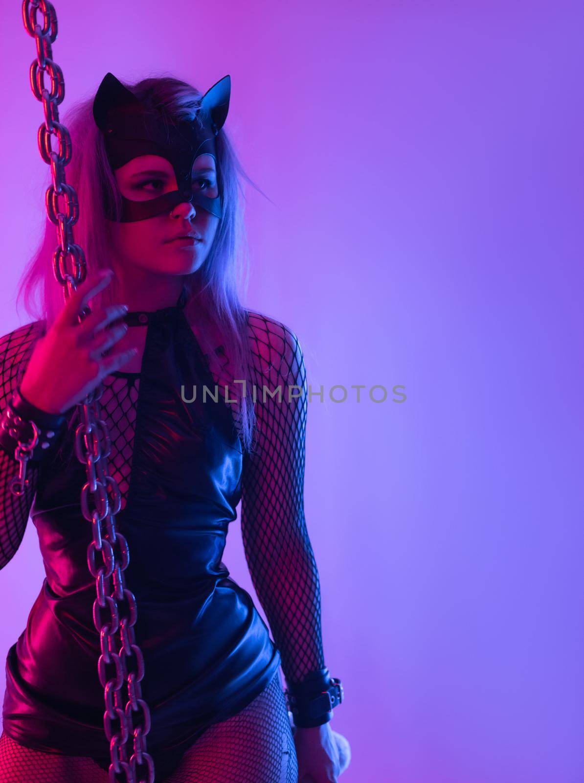 Sexy girl in latex dress bdsm mistress and cat mask in neon light with chains for sex games