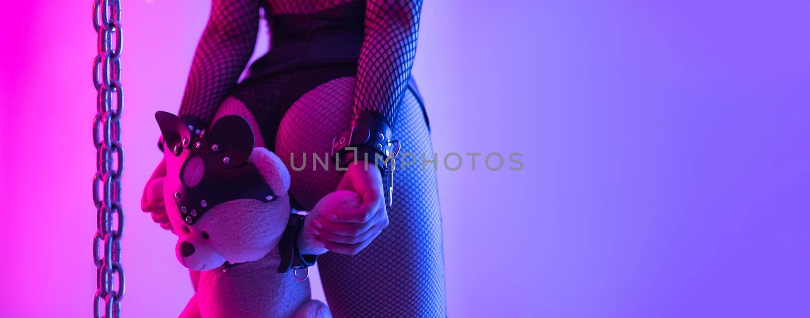 the buttocks of a sexy girl in leather bdsm handcuffs and a teddy bear in a mask and party dresses