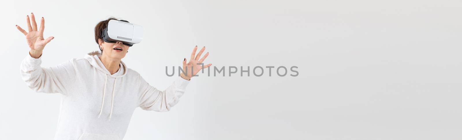 Modern technologies, future and people concept banner - Woman 40-50 years old wearing virtual reality glasses on white background with copy space and place for advertising by Satura86