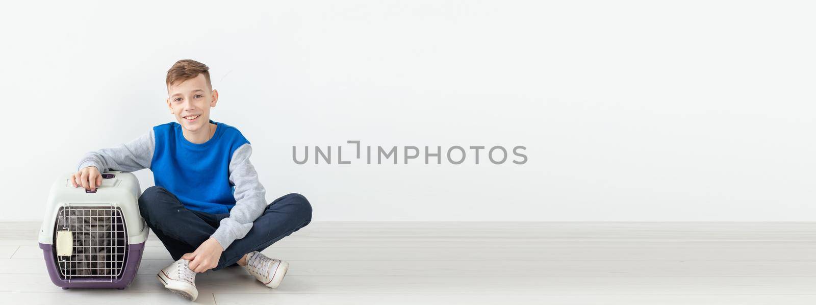 Laughing little positive boy holds a cage with a scottish fold cat next to him sitting on the floor in a new apartment banner with white background and copy space. Pet protection concept. by Satura86