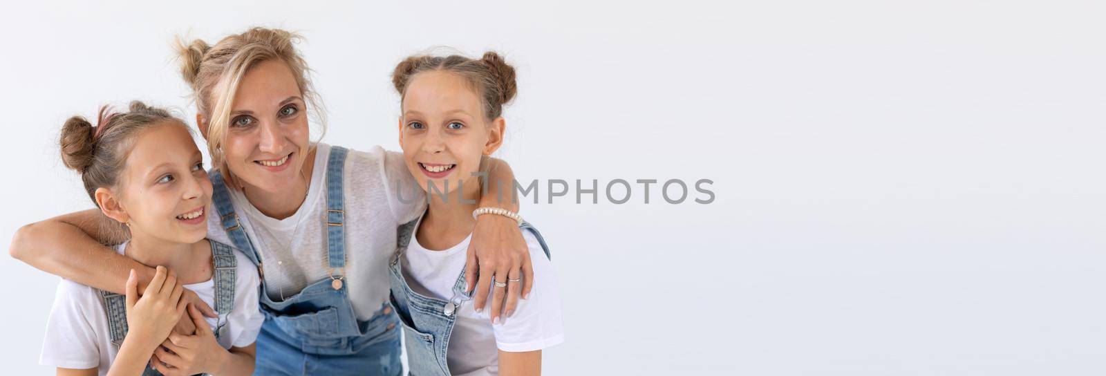 twins, family and children concept - portrait of a lovely mother embracing her twin daughters on white background banner with copy space and place for advertising by Satura86