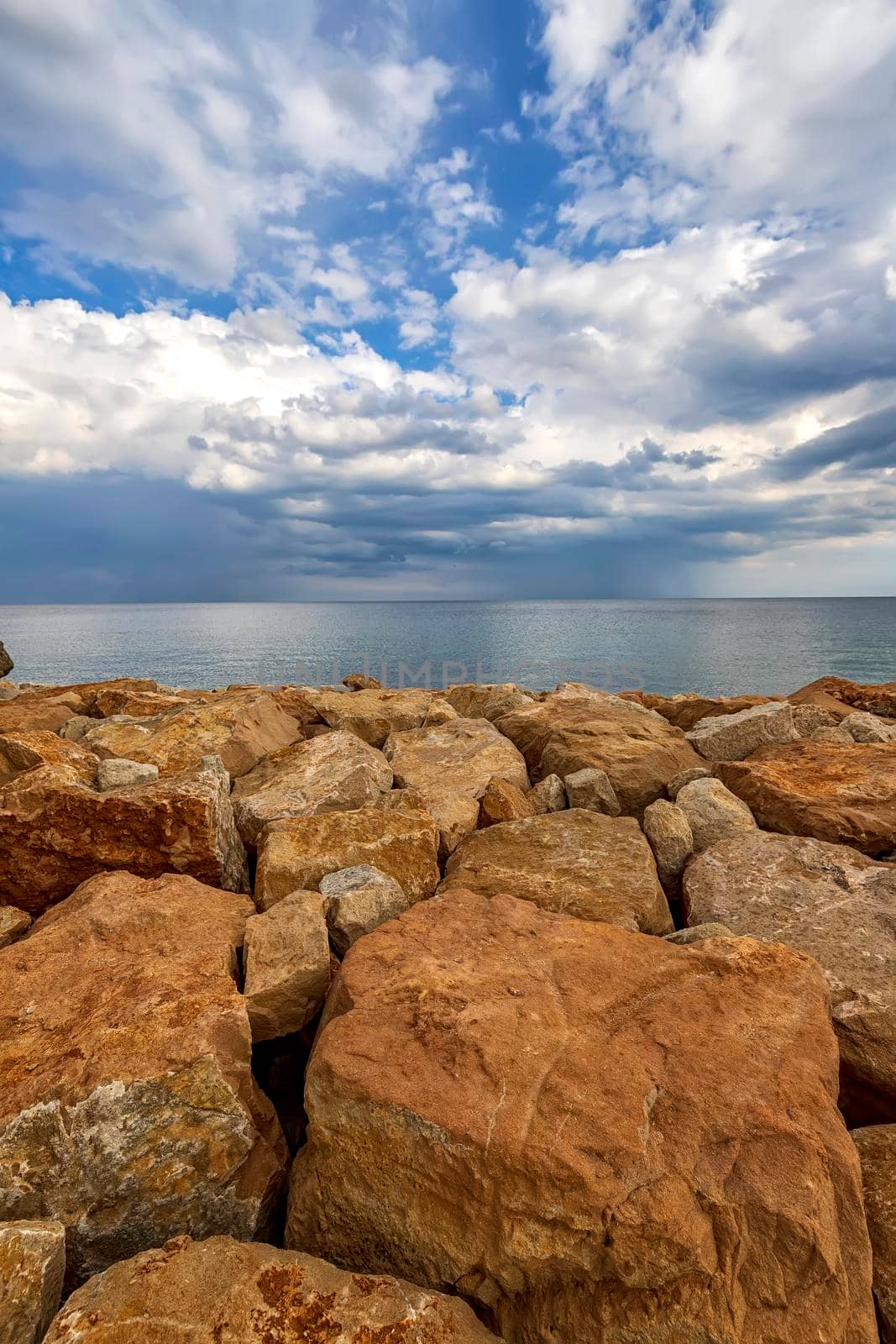Colorful stones on a shore with fluffy clouds at the horizon. Vertical view