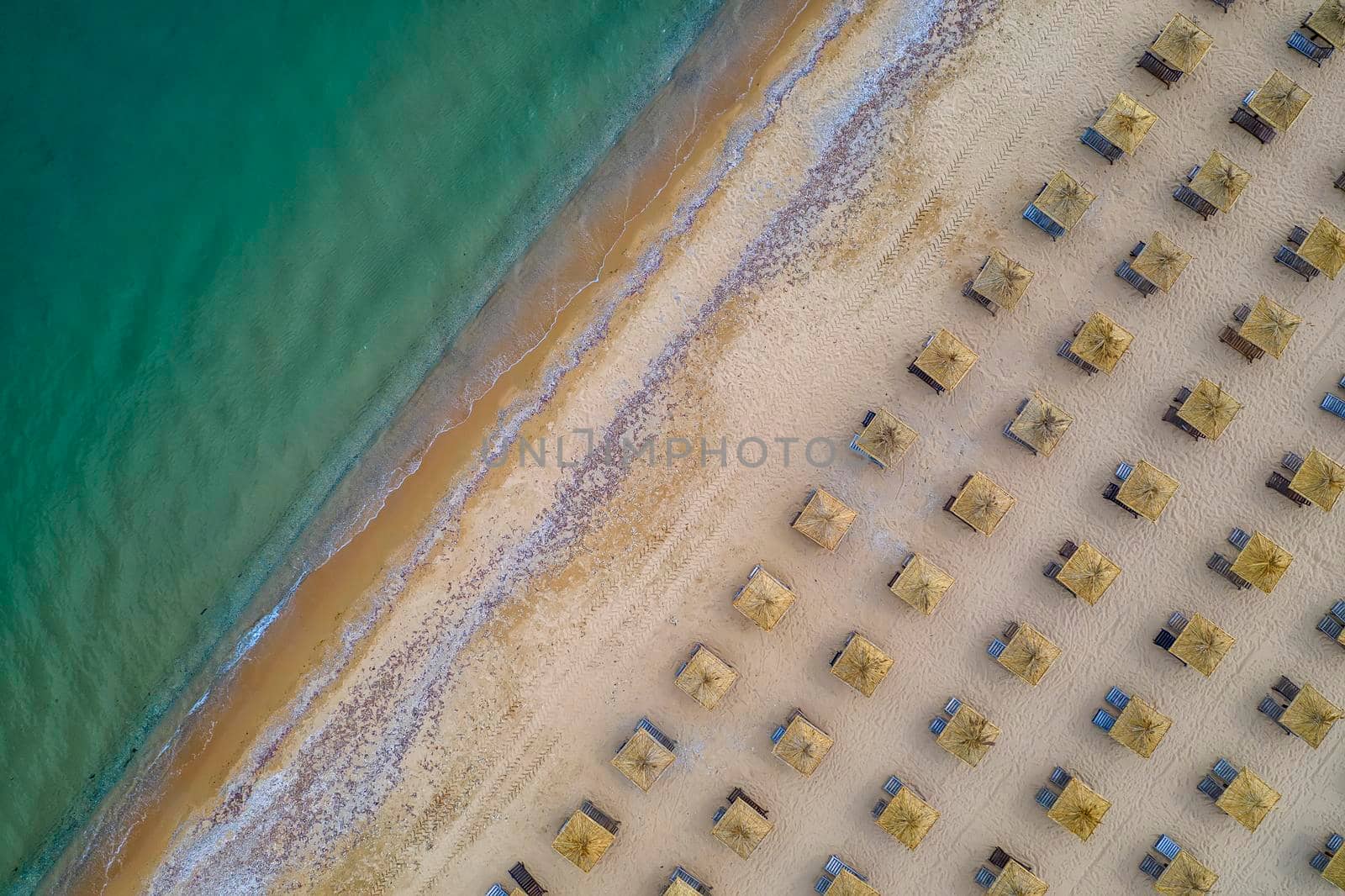 Aerial view of an amazing beach with wooden umbrellas, and calm sea. by EdVal