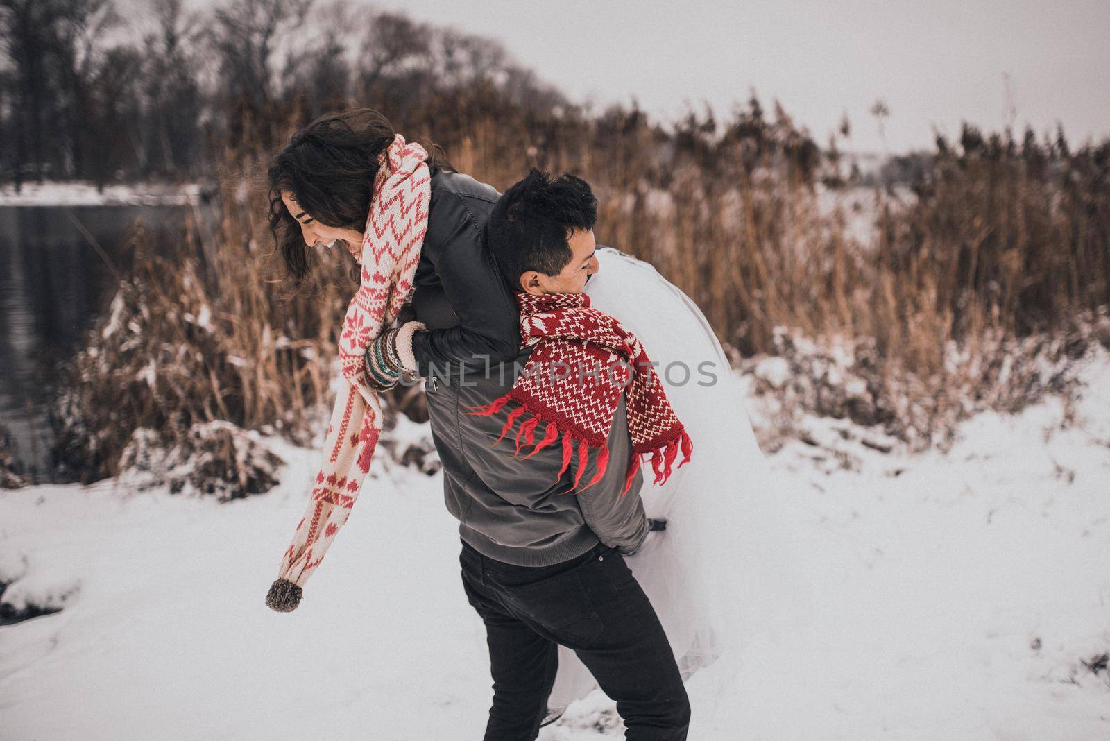 young man and woman running lying in the snow laughing fooling around having fun playing snowballs.bride and groom in love couple in knitted scarf and mittens in winter and snowflakes. mexican people