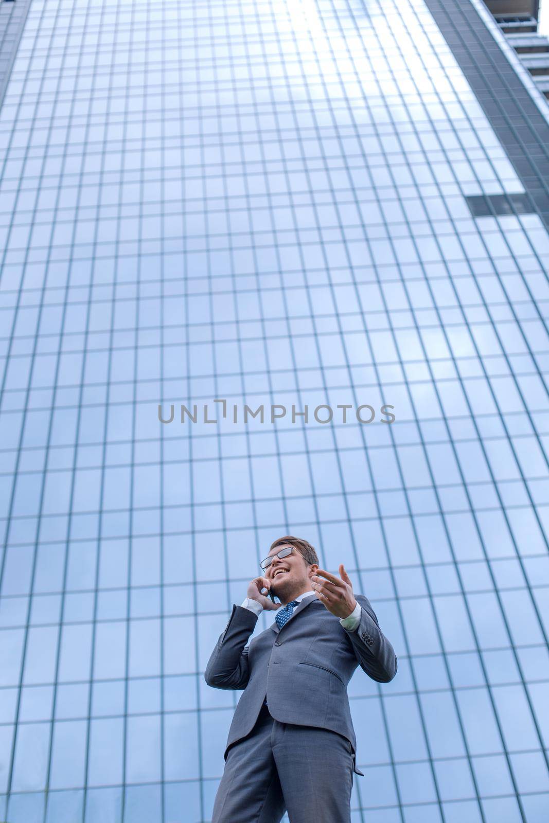 happy business man with smartphone standing in front of high rise office building by asdf